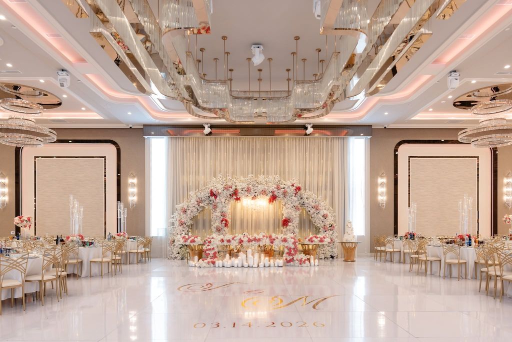 Ballroom with a floral arch of white and pink roses over the head table, candles and crystal chandeliers