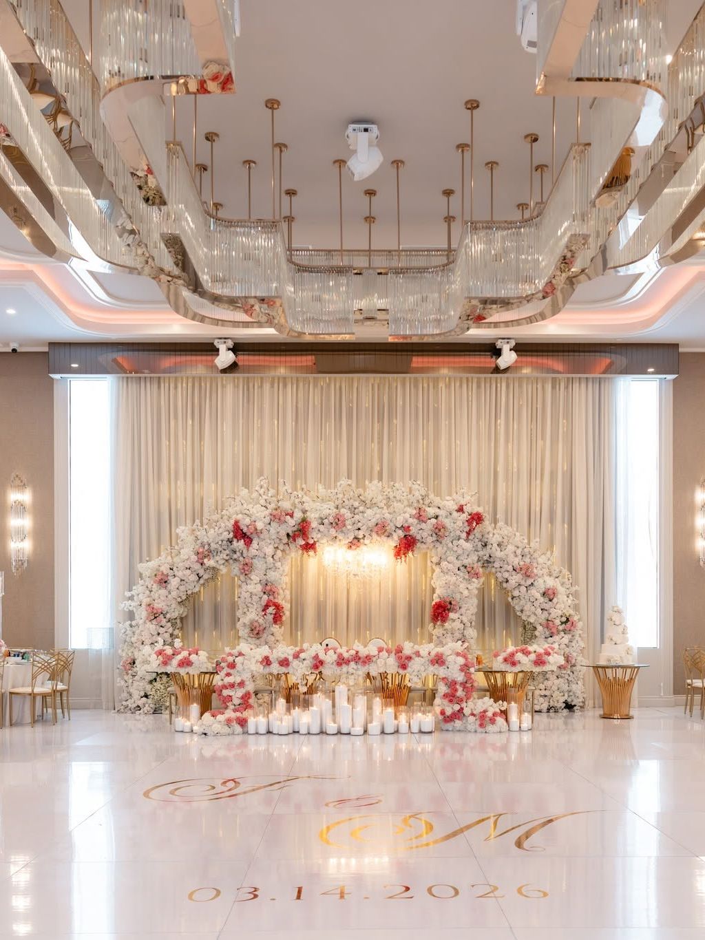 Floral arch of white and pink roses over a head table, with candles and a monogrammed dance floor