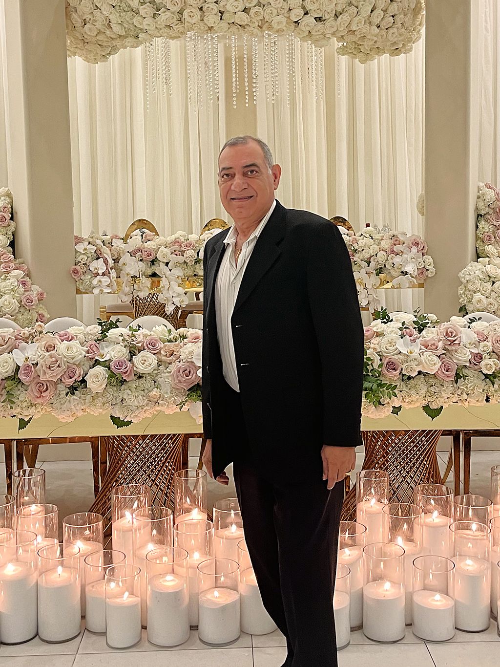 Joseph Hawara standing beside a candlelit floral head table he designed